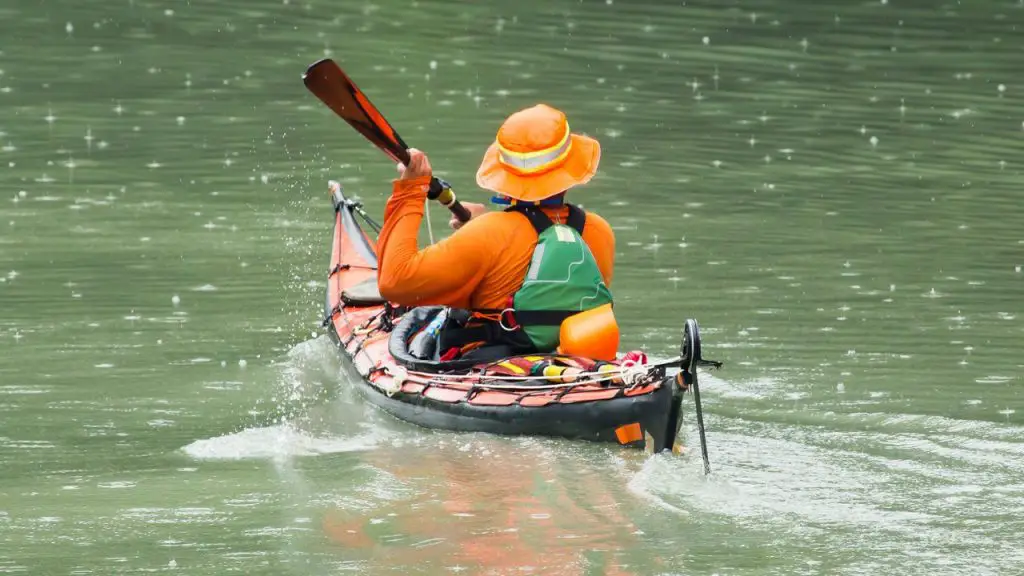  A girl wearing orange shirt is kayaking in the rain