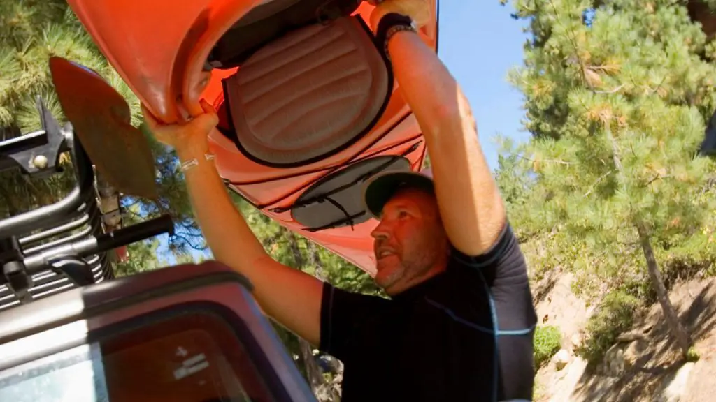 A man is putting Kayaks On Top of Vehicle