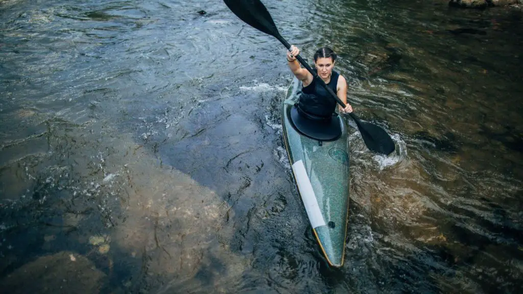 A woman is rowing a green kayak in a stream in the rain