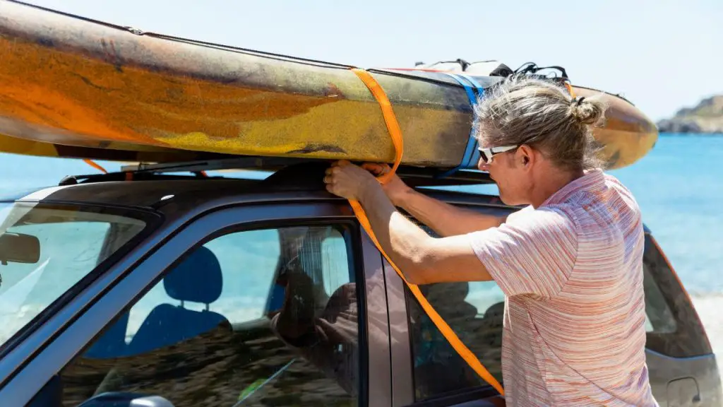 He is tying the kayak to the roof of the car