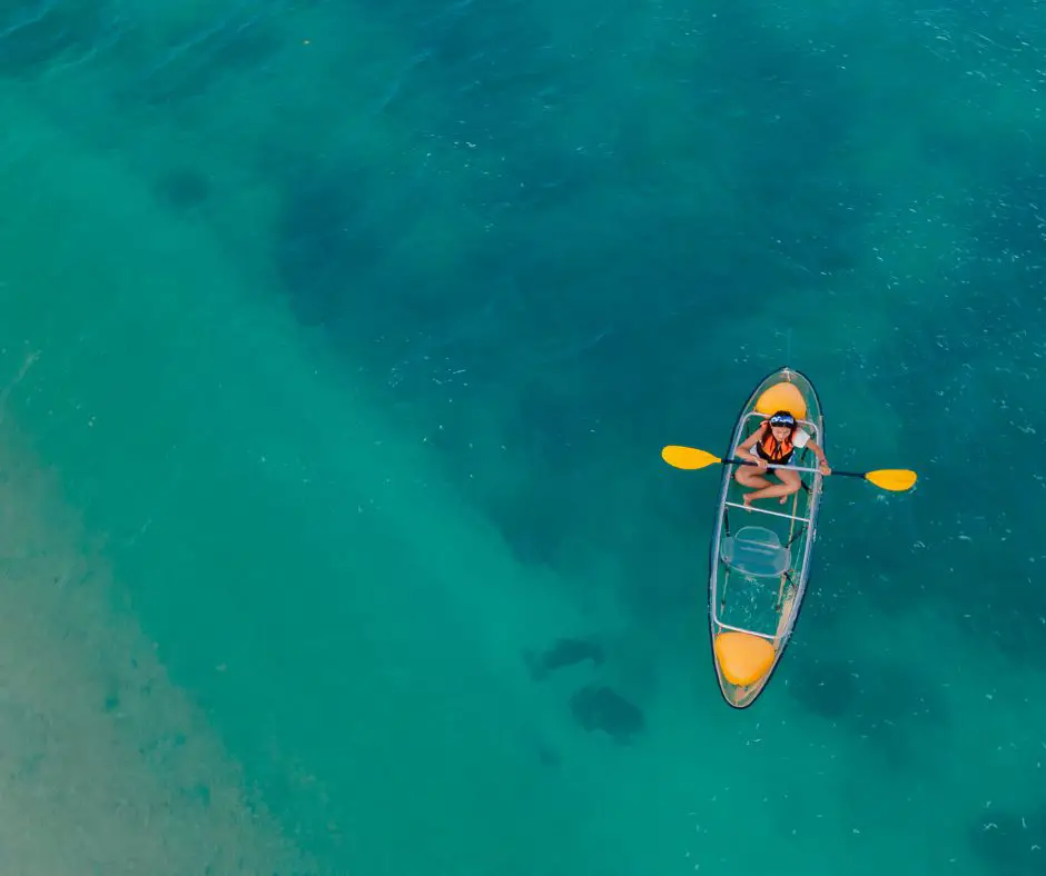 A girl is Paddling a transparent kayak in the sea