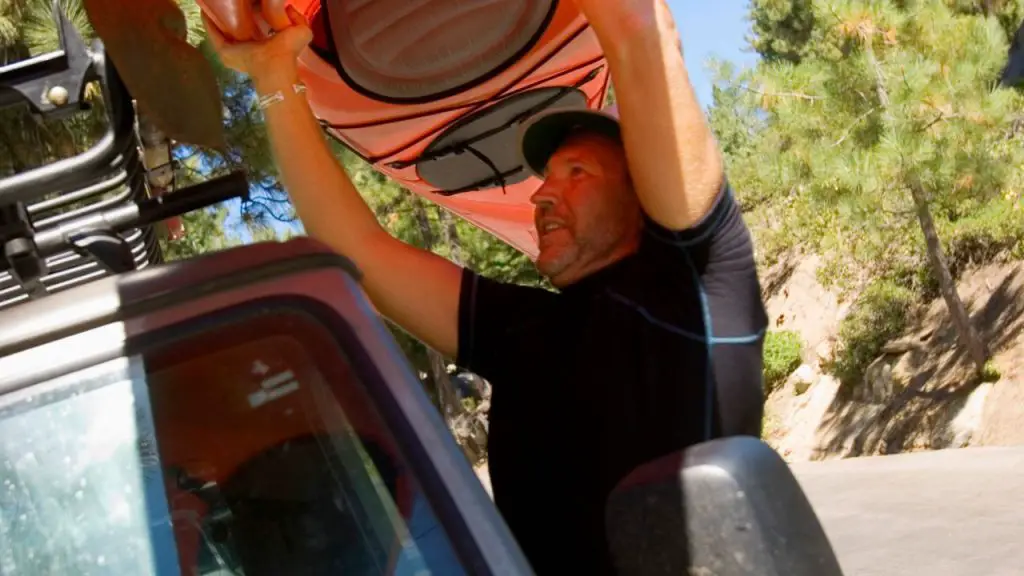 A man is carrying a kayak on roof top of a car