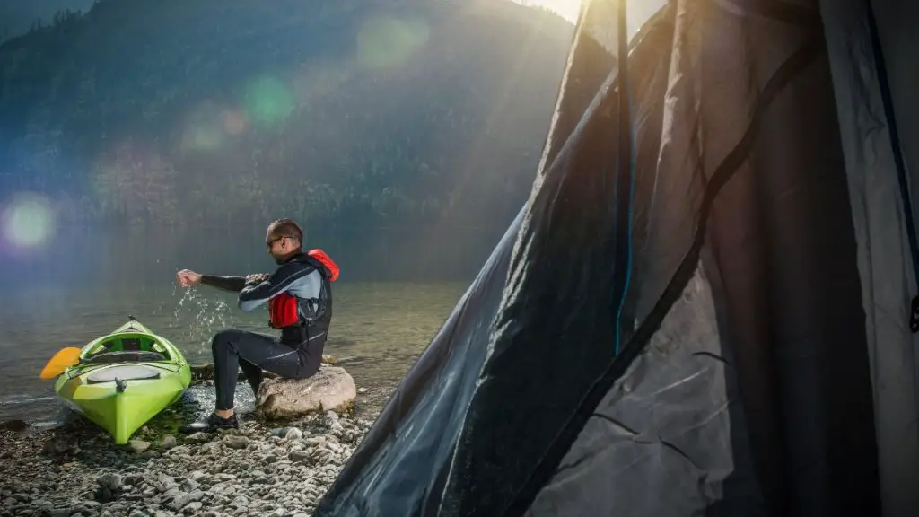 A man is sitting beside him kayak by the lake