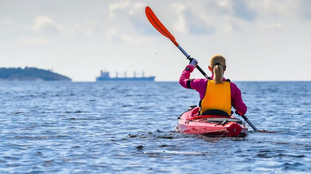 A woman is rowing red kayaking in the sea