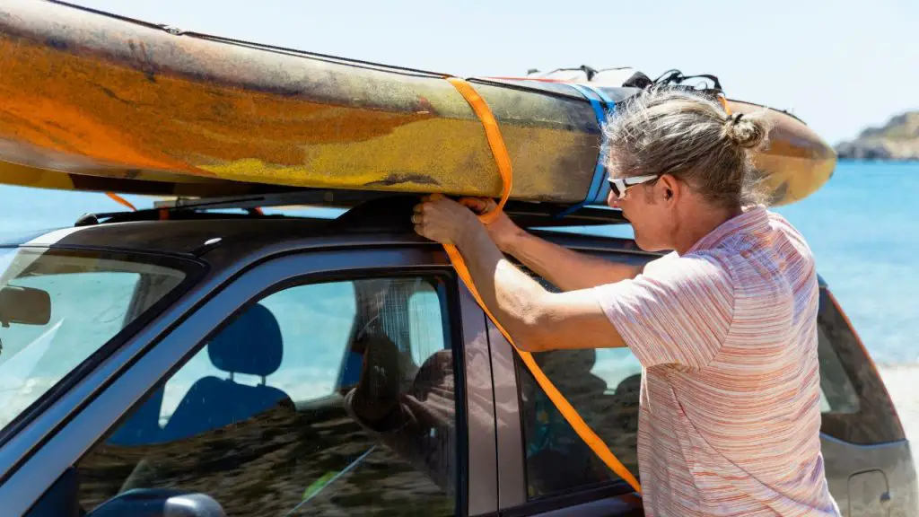 The man is tying a rope to fix the kayak on the roof of the car