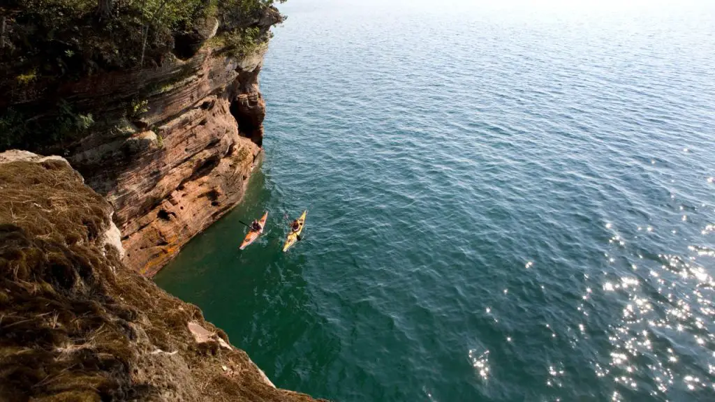 Two kayaks are paddling near the cliff in the sea
