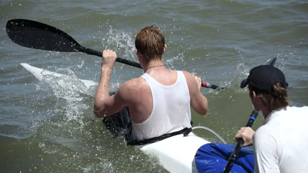 A kayak is loading with 2 men and some water in the cockpit