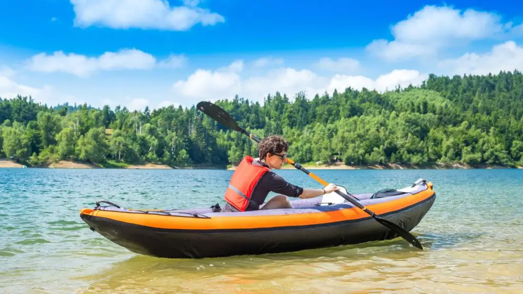 A man is getting out of an inflatable kayak.