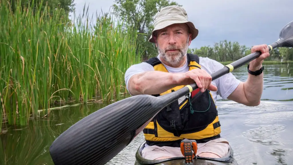 A man is paddling a sit-in kayak with carbon paddle