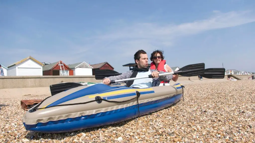 a couple sitting on an inflatable kayak on the beach with small stones