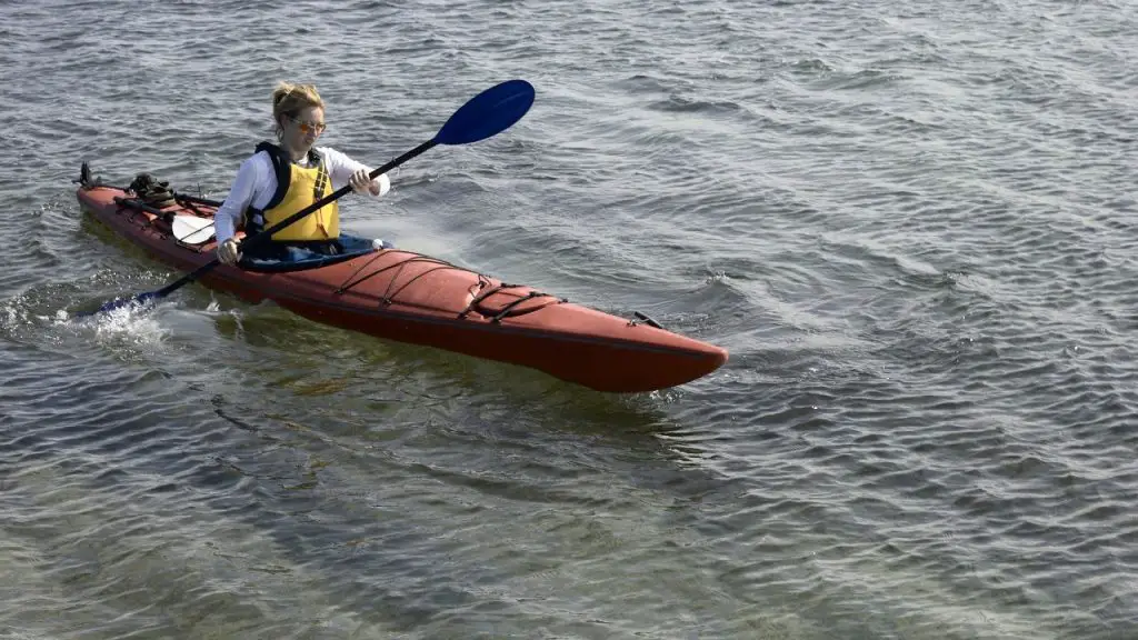 A girl is padding kayak along the side of the river.