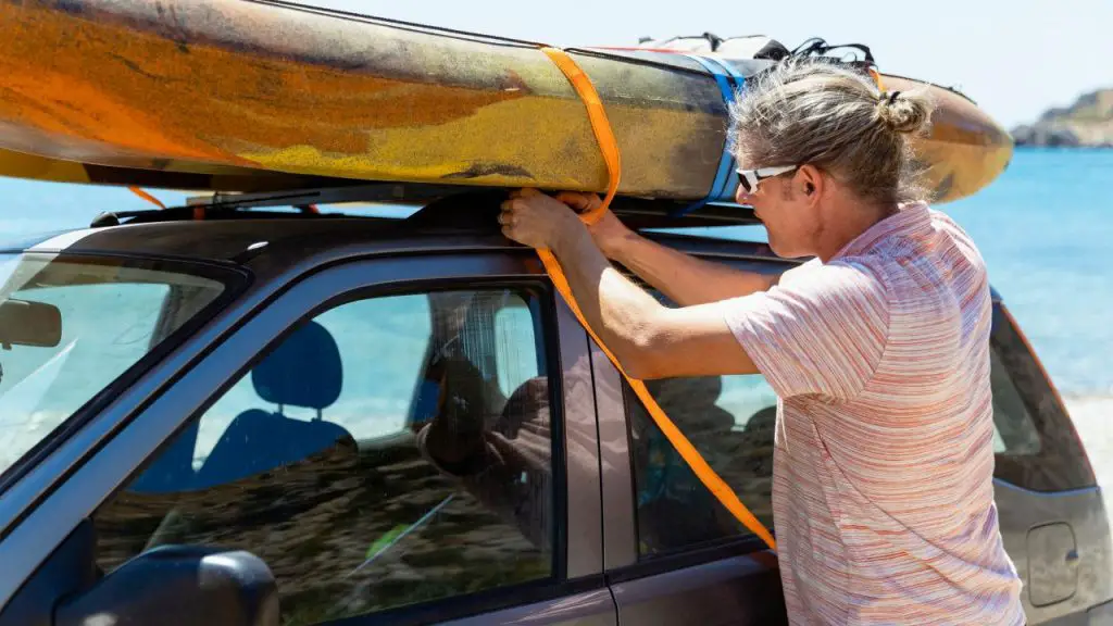 A man is Tying Down kayak on roof car