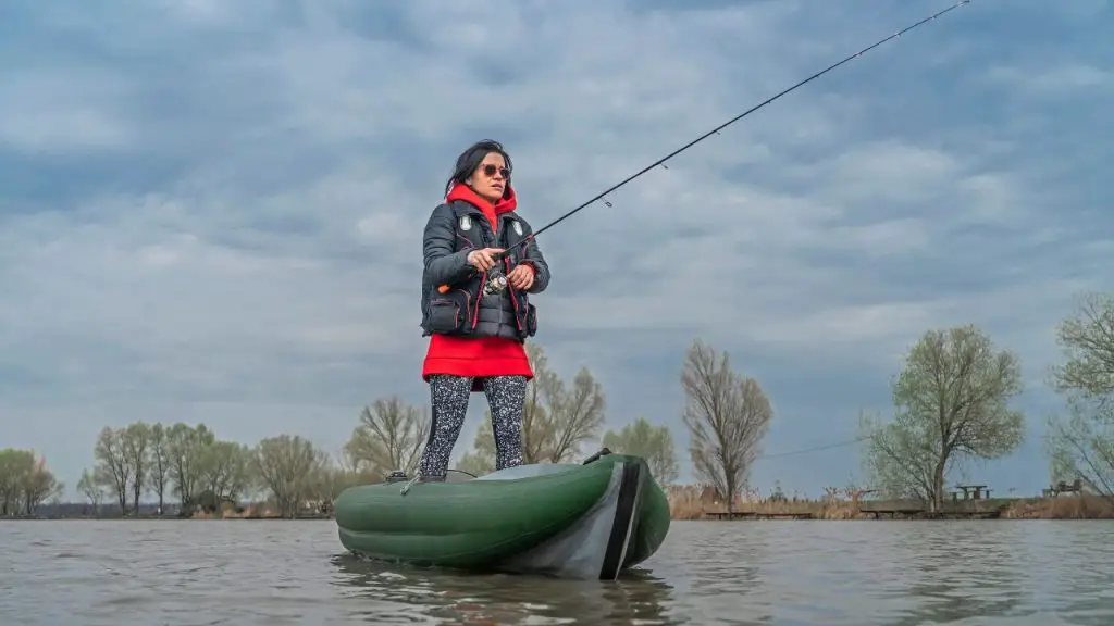 a girl is standing fishing on an inflatable kayak